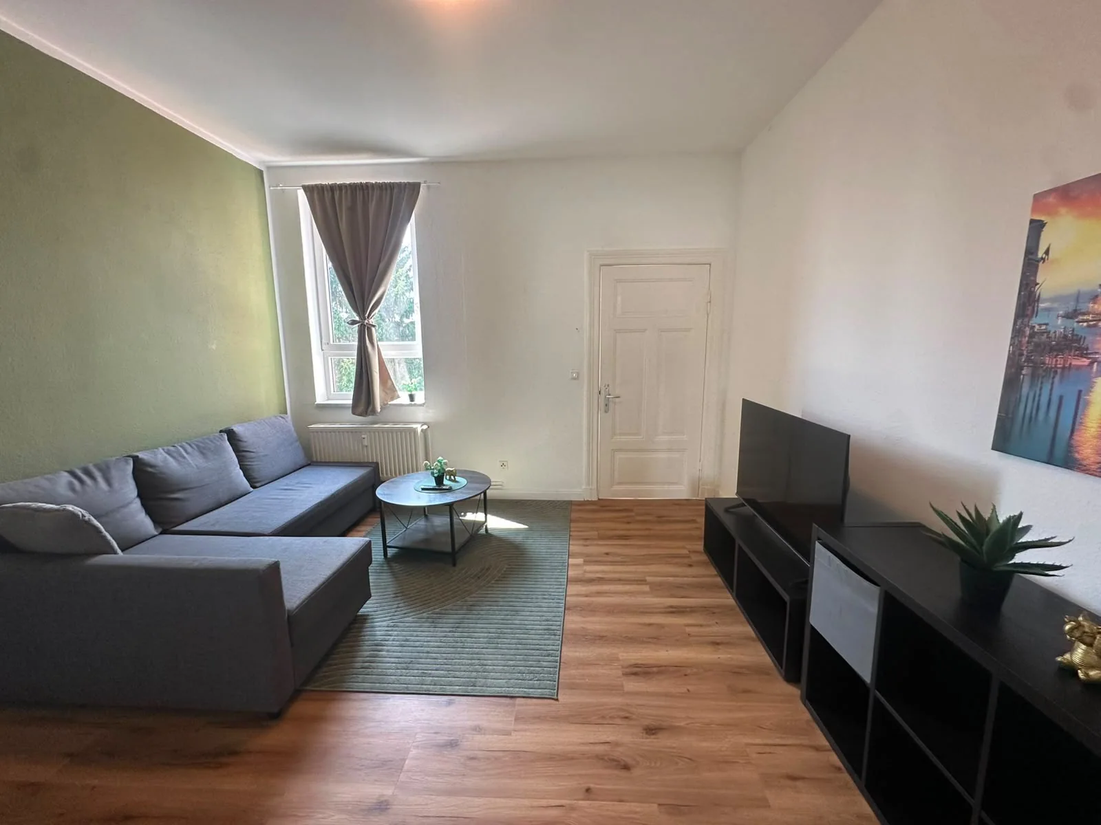 Wohnzimmer mit grauem Ecksofa, grüner Wand und Fernseher